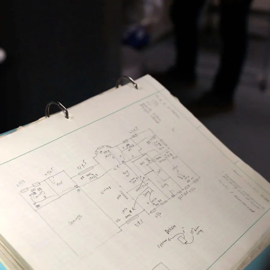 Person holding pen and reviewing detailed architectural or engineering plans in a binder with diagrams.