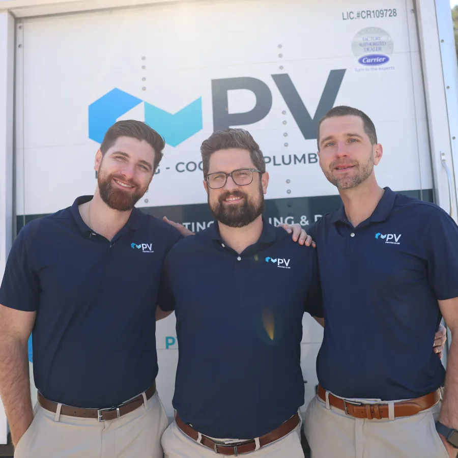Three men in branded navy blue shirts standing and smiling in front of a company truck with PV logo.