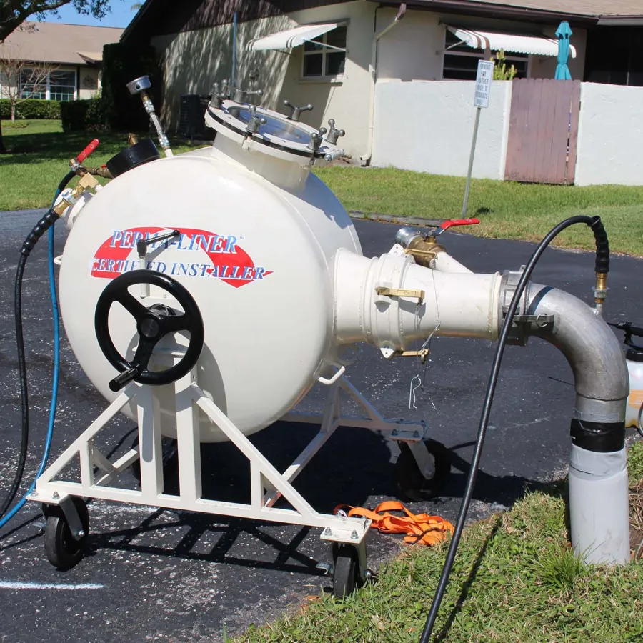 Portable pressurized pipe lining machine connected to a residential sewer pipe outdoors.
