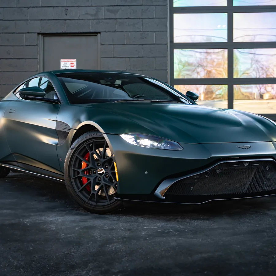 Dark green Aston Martin sports car parked indoors with sleek design and illuminated headlights.