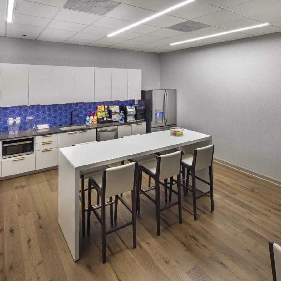 Modern office kitchen with white cabinets, blue tile backsplash, wooden floor, and island with four chairs.