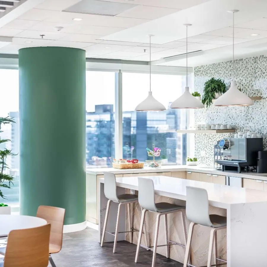 Modern office kitchen with marble island, bar stools, green column, mosaic backsplash, and city view windows