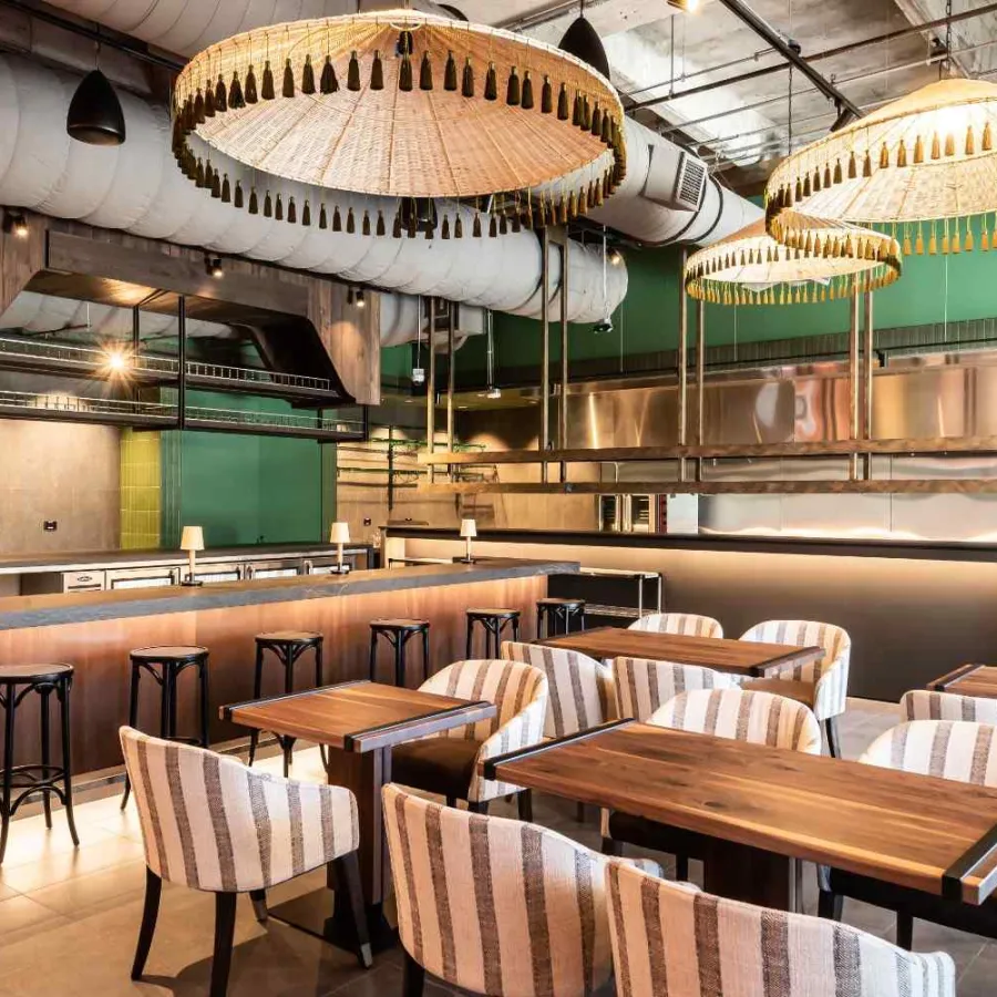 Modern restaurant interior with wooden tables, striped upholstered chairs, and large tassel pendant lights.