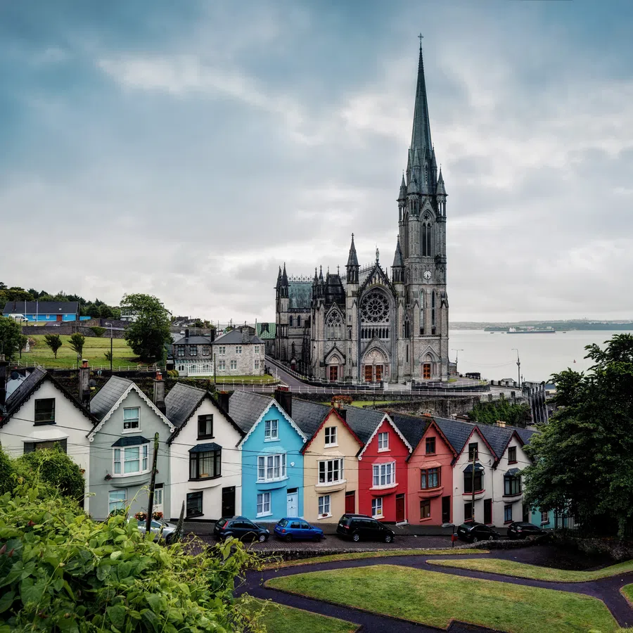 Colorful row houses with Gothic-style church and overcast sky in a coastal town landscape.