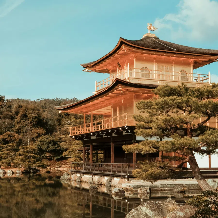 Golden Pavilion temple reflecting in calm water surrounded by trees under a clear blue sky.