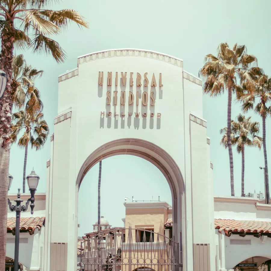 Entrance arch of Universal Studios Hollywood framed by palm trees and vintage street lamps under clear sky.