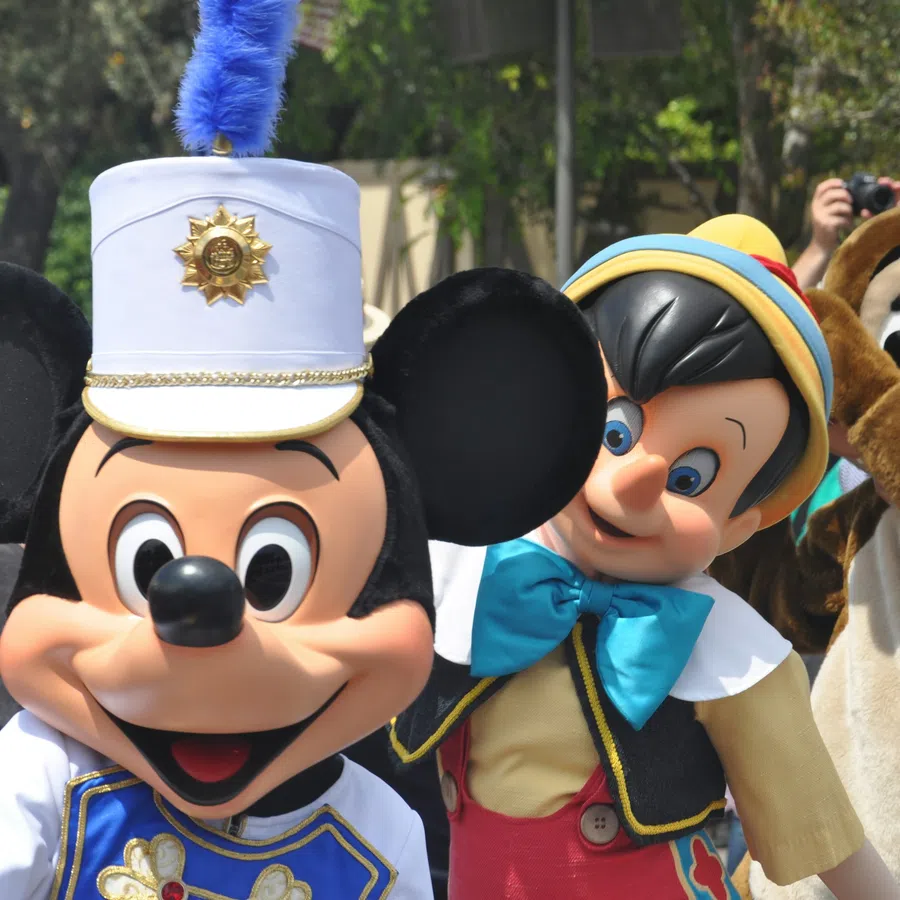 Mickey Mouse dressed as a band leader with Pinocchio and Chip mascot characters posing at a theme park event.