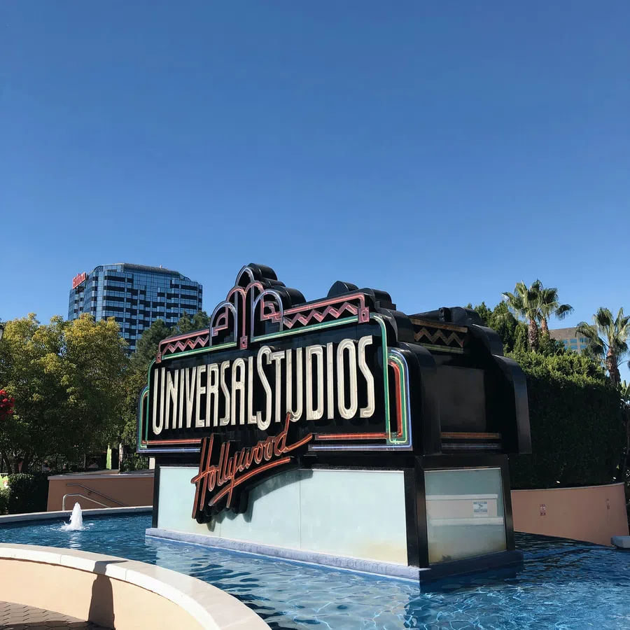 Universal Studios Hollywood sign above a water feature with clear blue sky and palm trees in the background