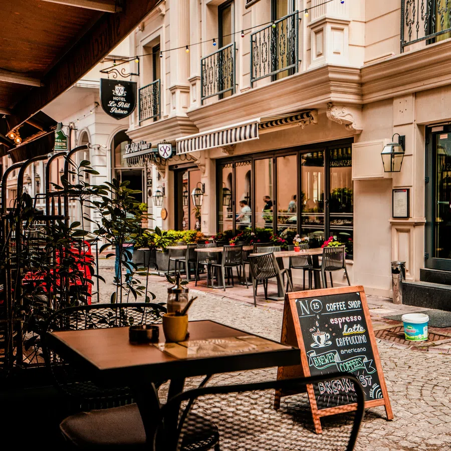 Cozy outdoor café seating with tables, chairs, and a menu board on a cobblestone street in a historic city area.