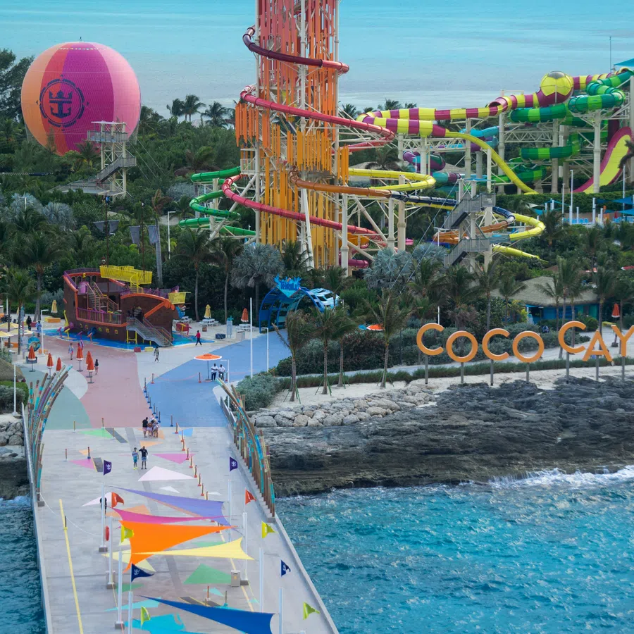 Colorful waterpark with slides, tower, and signage at Coco Cay island beside turquoise sea and walkway.