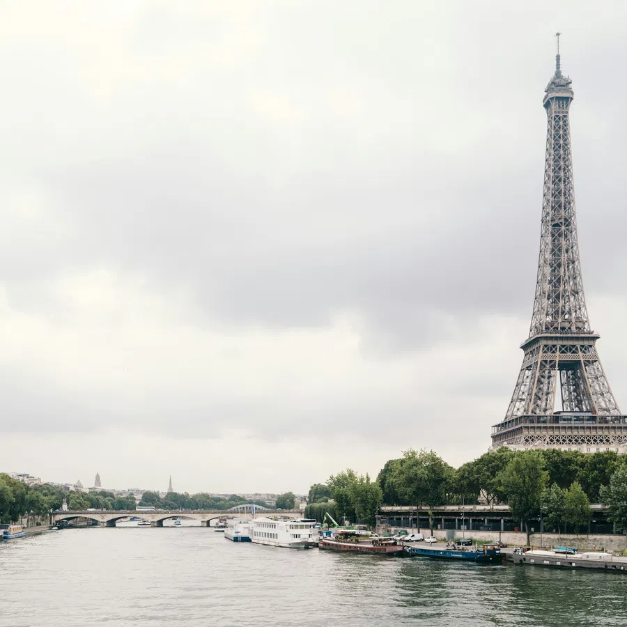 Eiffel Tower beside the Seine River with boats and cloudy sky in Paris cityscape.
