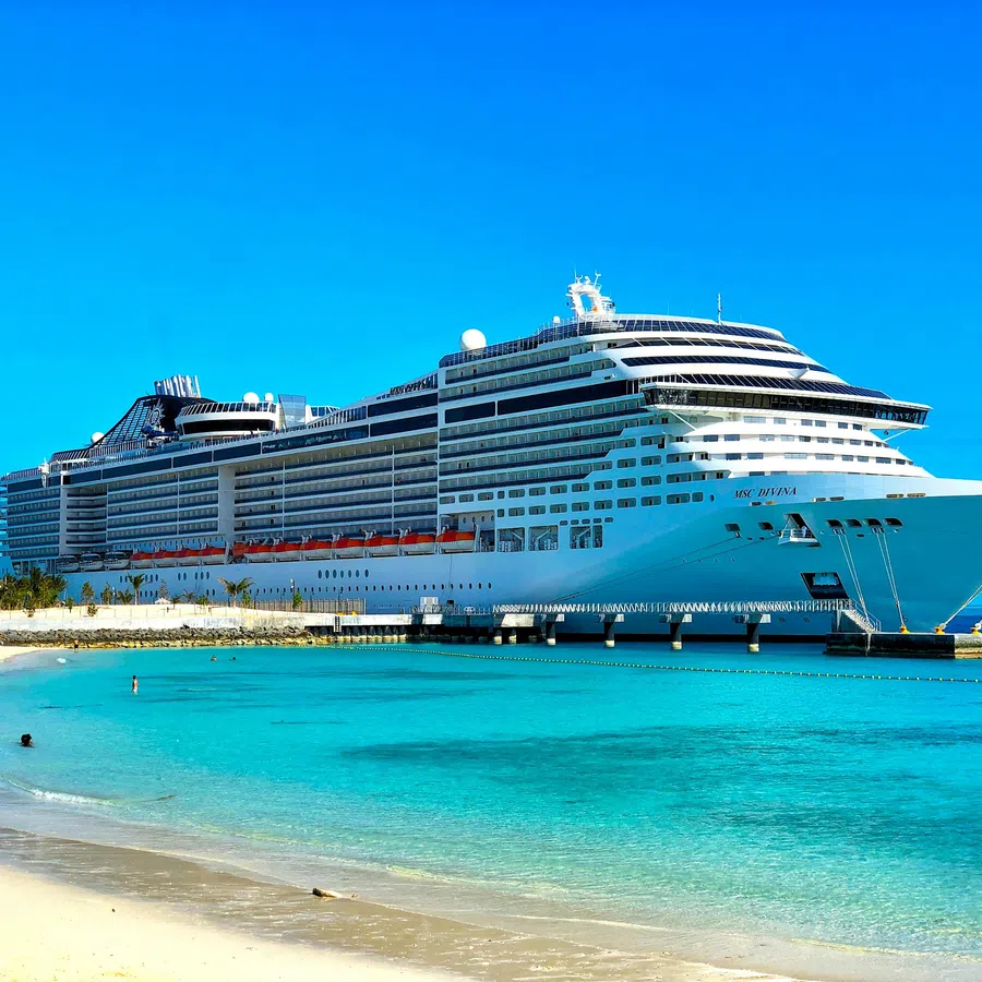 Large white cruise ship docked at a tropical beach with turquoise water and clear blue sky