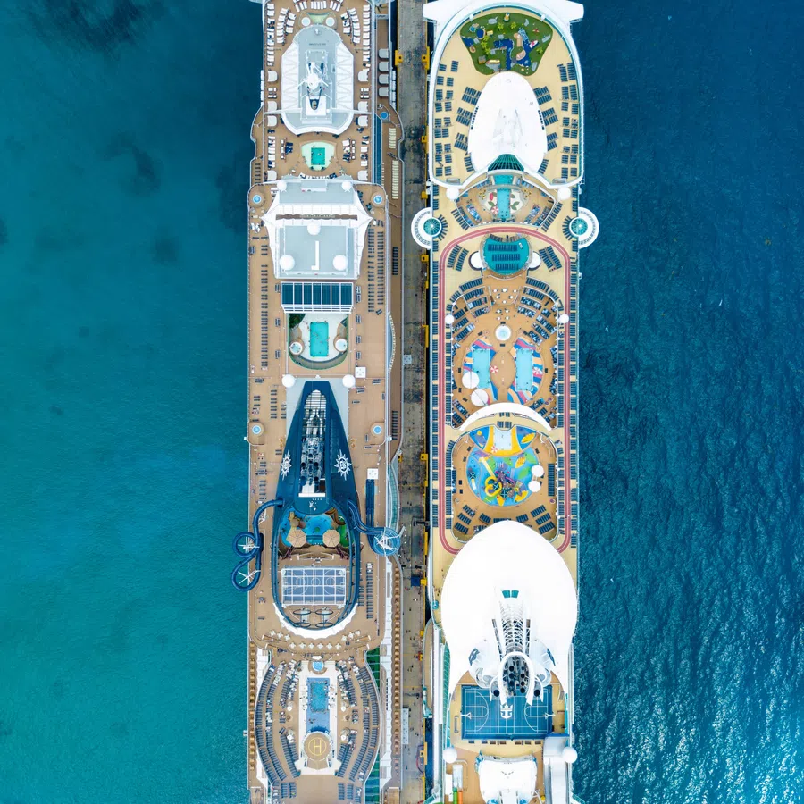 Aerial view of two large cruise ships docked side by side in clear blue ocean waters.