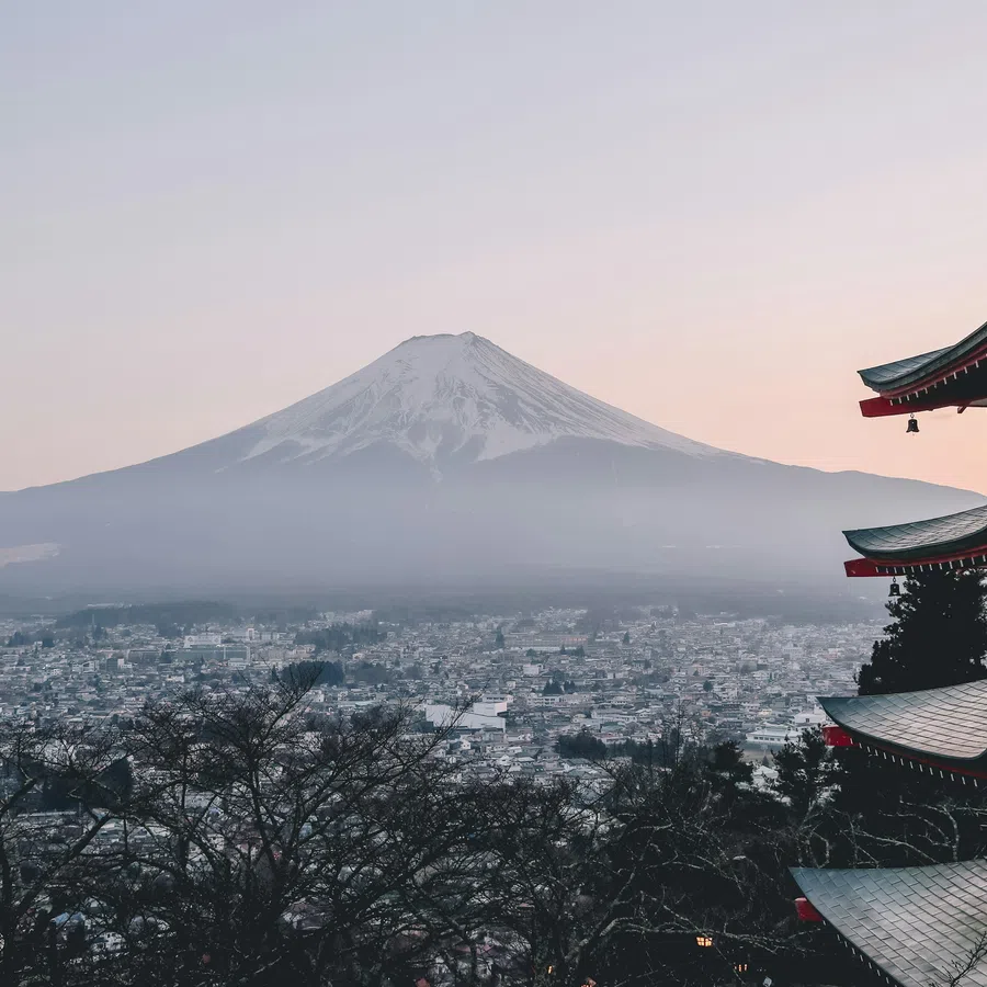 Pagoda overlooking a city with Mount Fuji in the background at dawn, misty and serene landscape.