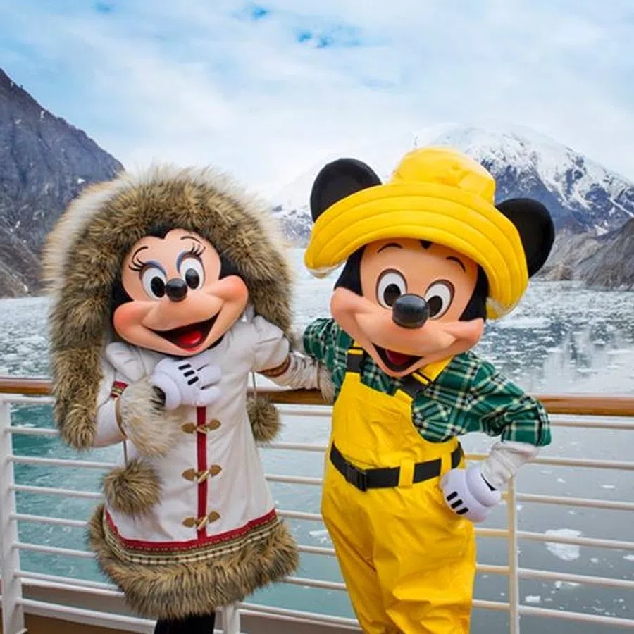 Mickey and Minnie Mouse dressed in winter clothes posing on a ship deck with icy mountains and water in the background.