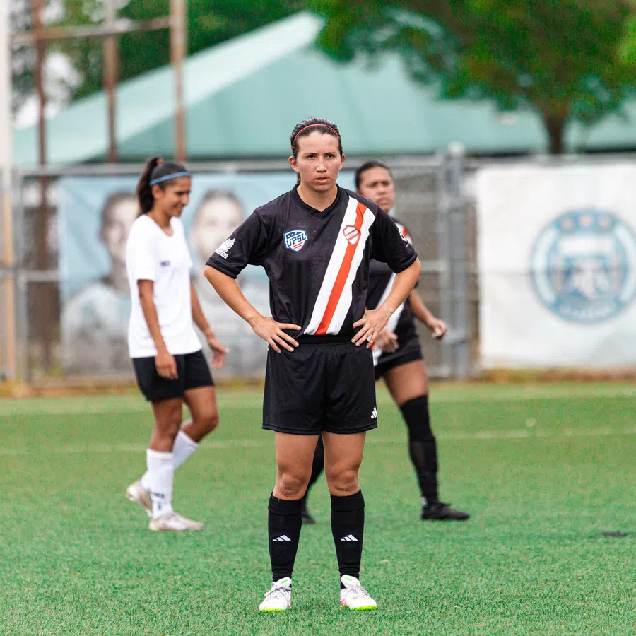 Female soccer players on a green field during a game, with one player in black uniform in focus.