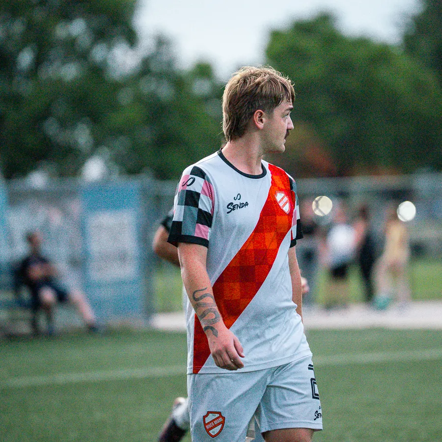 Soccer player in white and red uniform standing on a green field during a game with blurred spectators in background