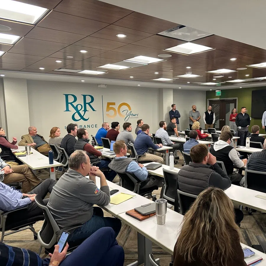 Office team attentively listening to speaker during a training session at R&R Insurance celebrating 50 years.