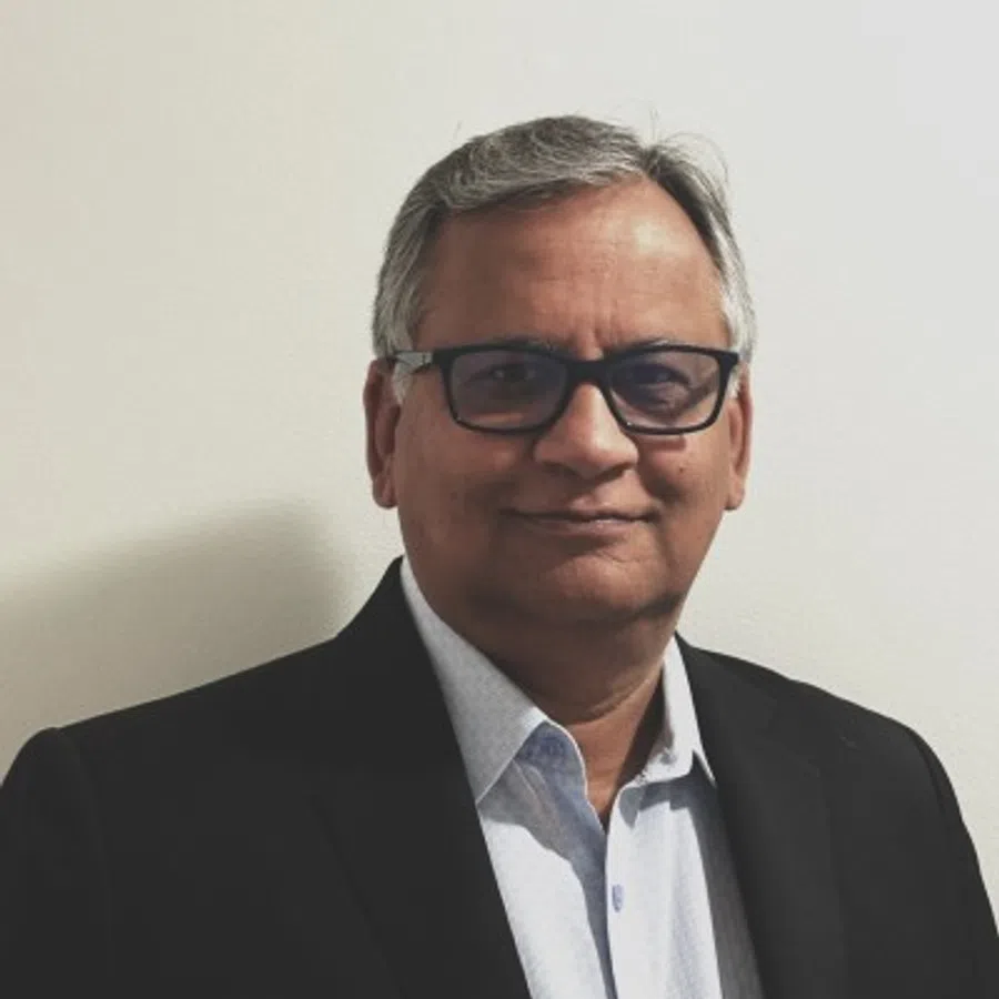 Middle-aged man with gray hair and glasses wearing a black blazer and light blue shirt against a white background