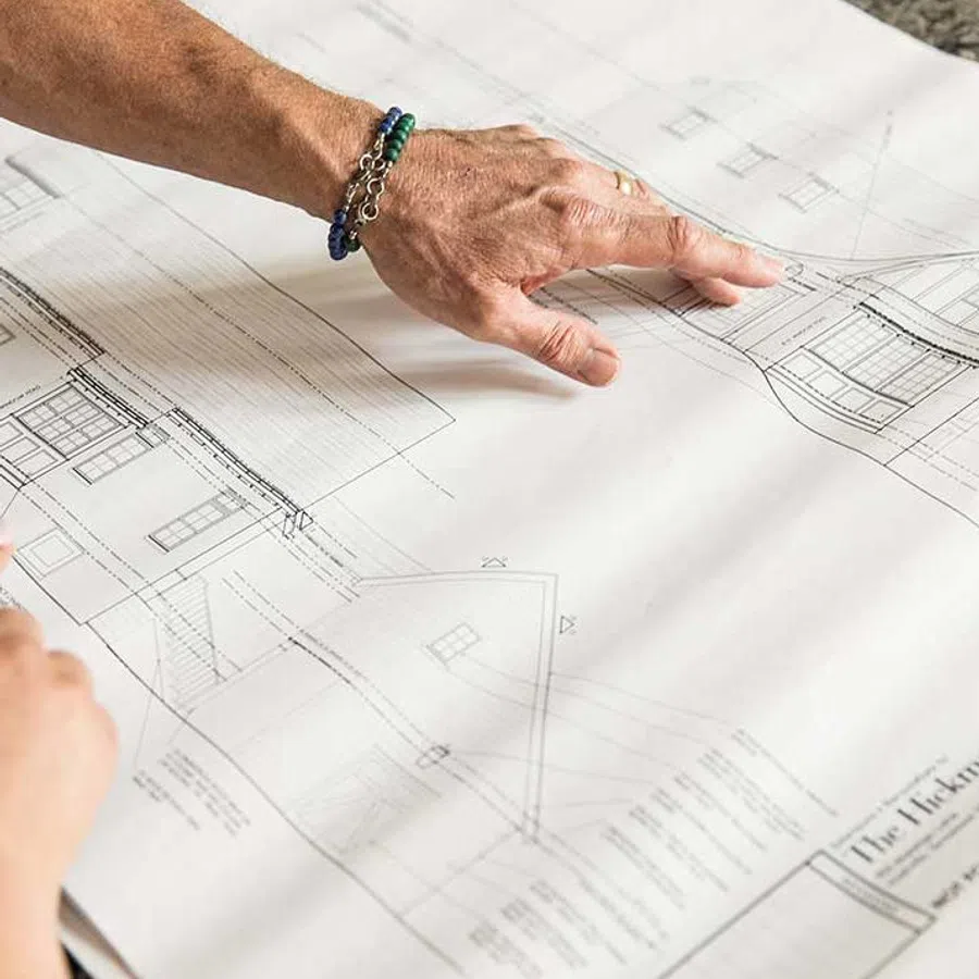 Hand pointing to architectural blueprints of a house with detailed design and structural plans.