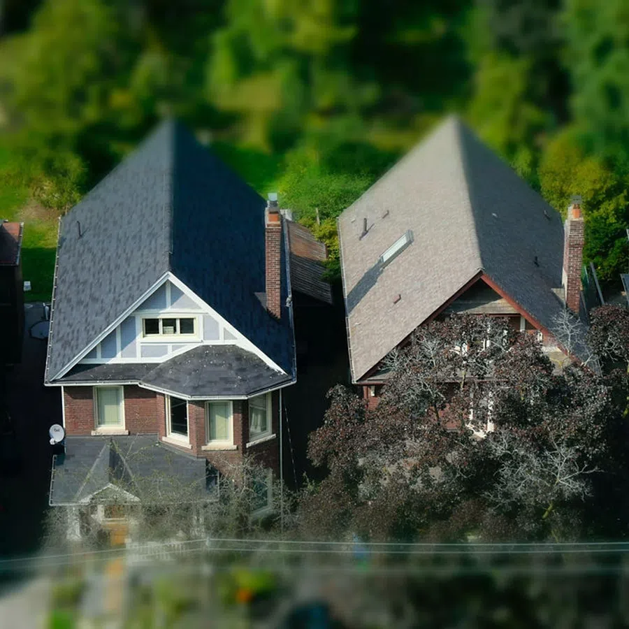 Aerial view of four closely spaced suburban houses with varied roof styles and greenery around.