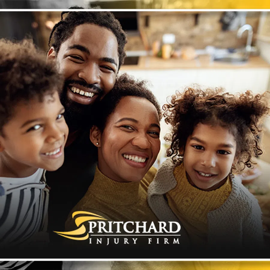 Smiling happy family of four posing indoors with Pritchard Injury Firm logo at the bottom center.