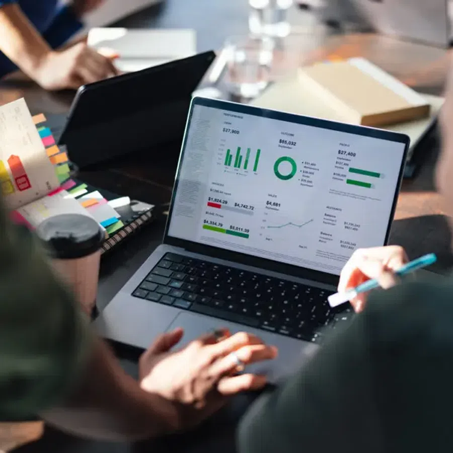People analyzing business data and charts on a laptop during a collaborative meeting at a table.
