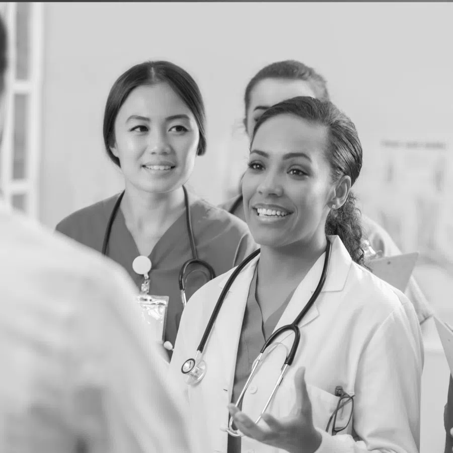 Diverse group of medical professionals discussing patient care in hospital setting, wearing scrubs and stethoscopes.