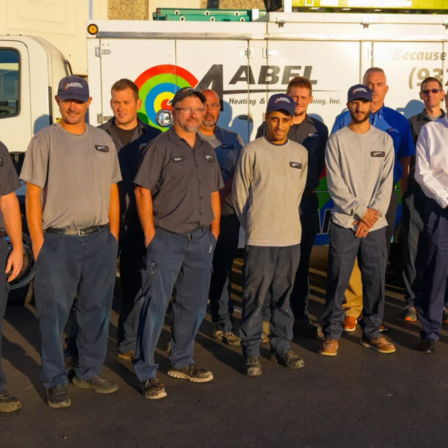 Team of Abel Heating and Cooling employees standing in front of a service truck with company logo in sunlight