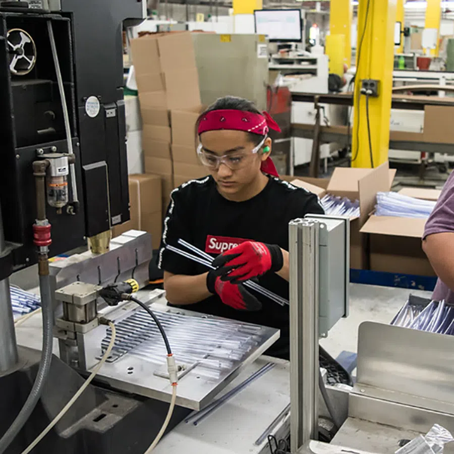 Factory workers assembling metal parts on a production line with machinery and packing boxes in the background