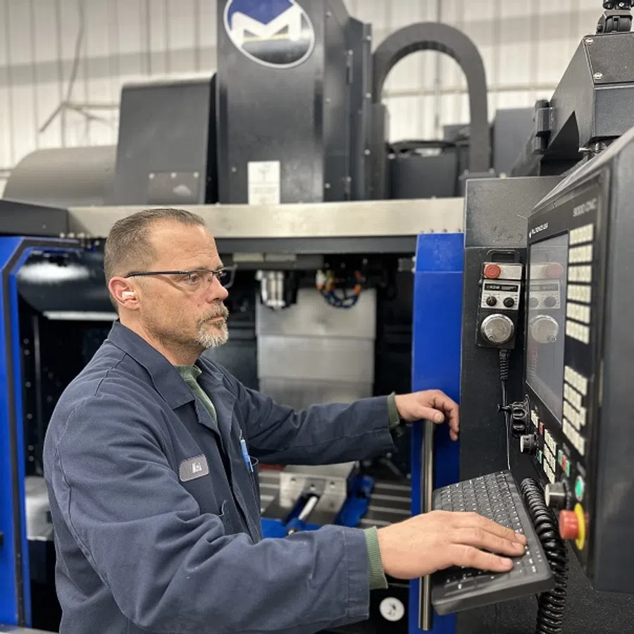 Technician operating a CNC machine, using control panel in a metal fabrication workshop.