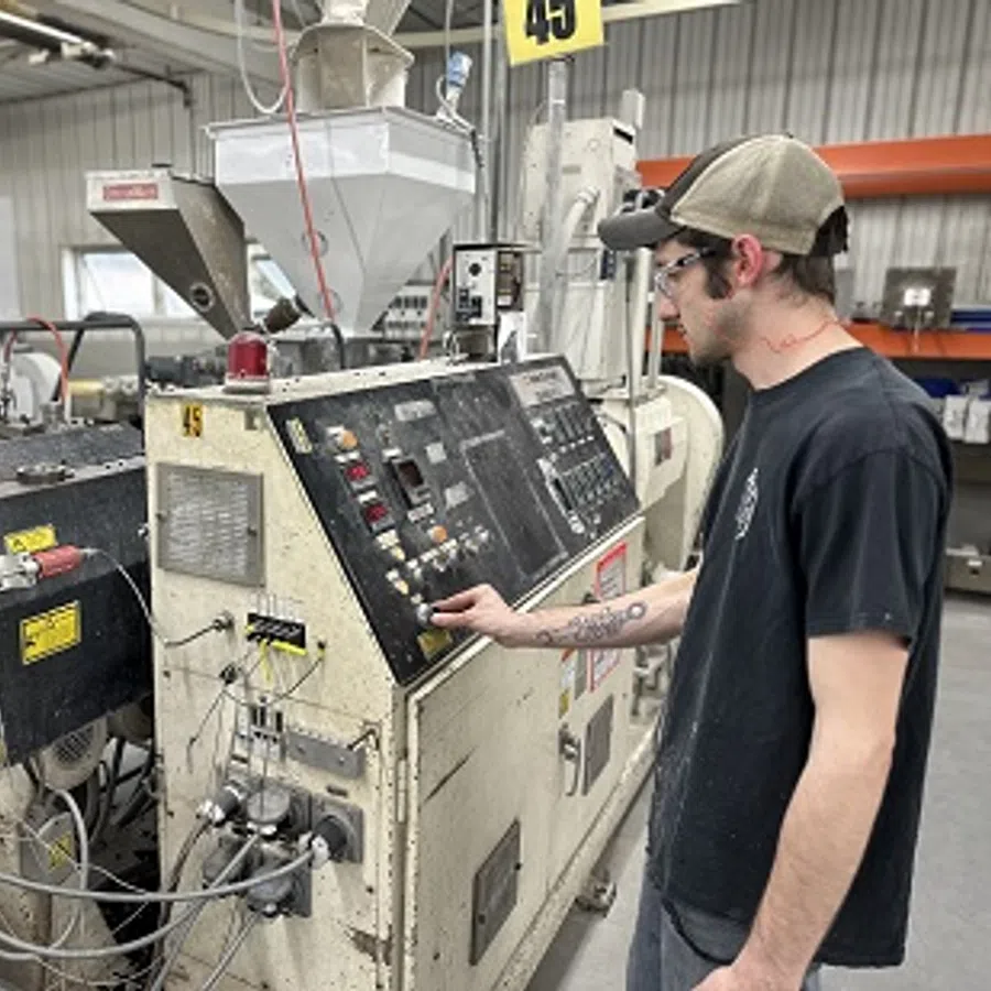 Worker operating industrial injection molding machine in a manufacturing facility with safety glasses and cap