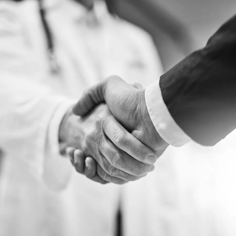 Black and white close-up of a handshake between a doctor and a businessperson symbolizing trust and partnership.