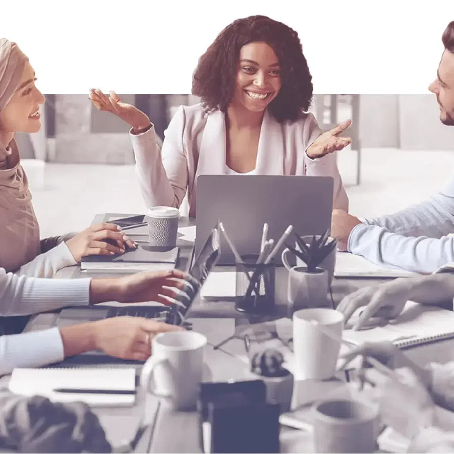 Diverse colleagues collaborating and discussing ideas around a table with laptops and coffee cups in a modern office.