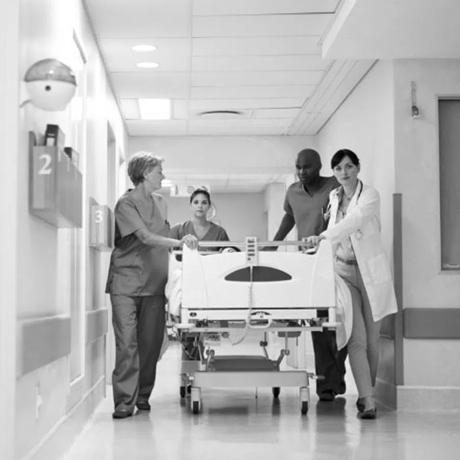 Healthcare professionals transporting a patient on a hospital bed through a corridor, working collaboratively.