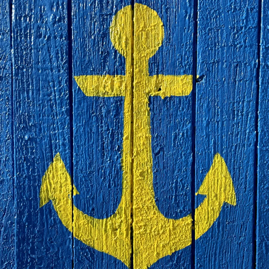Yellow anchor painted on textured blue wooden planks symbolizing maritime or nautical theme.