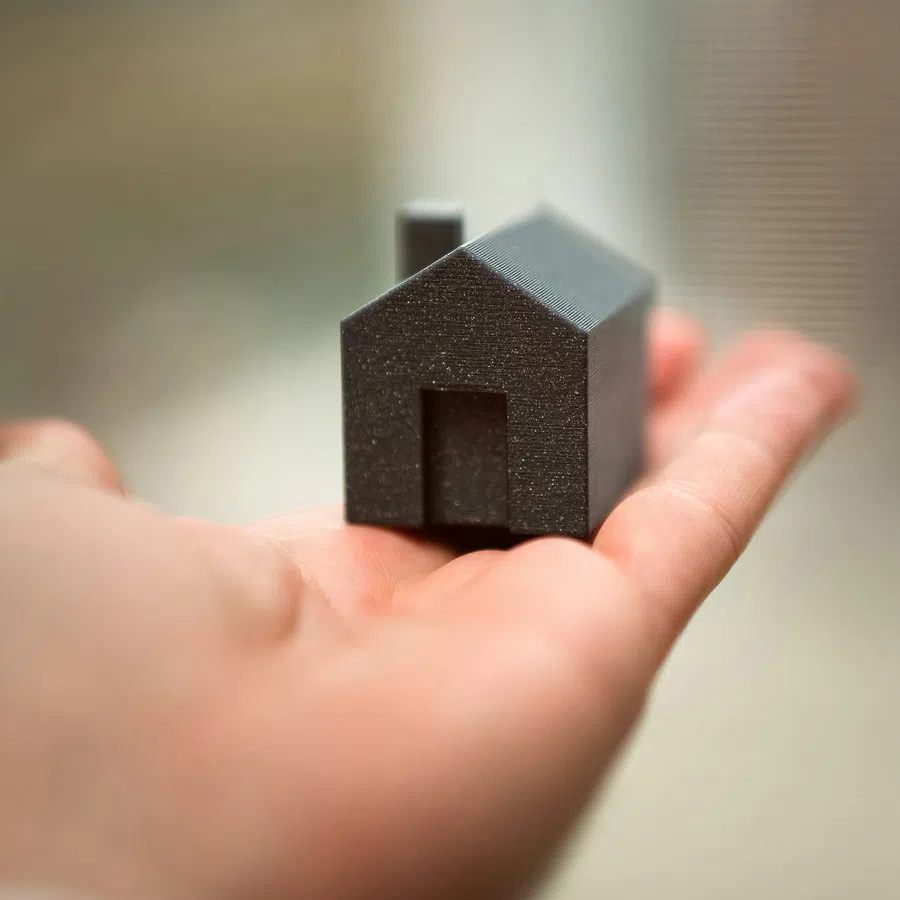 Hand holding a small black house model on blurred background symbolizing real estate or home ownership.