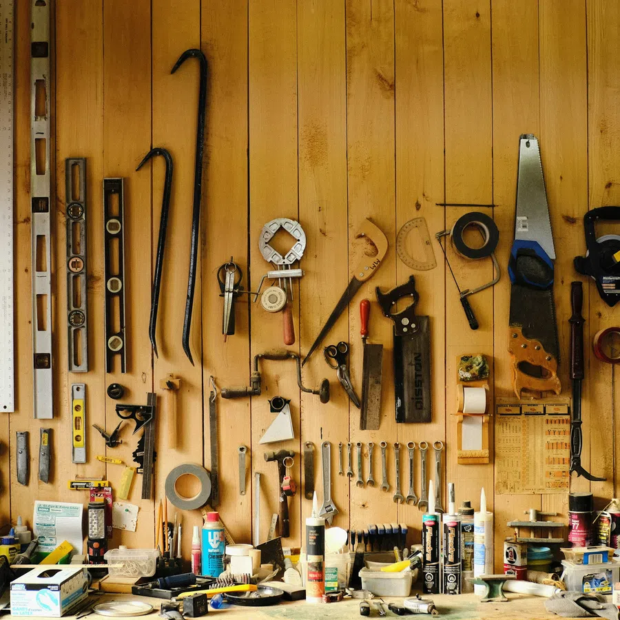 Wooden wall with an assortment of hanging hand tools and measuring instruments in a workshop.