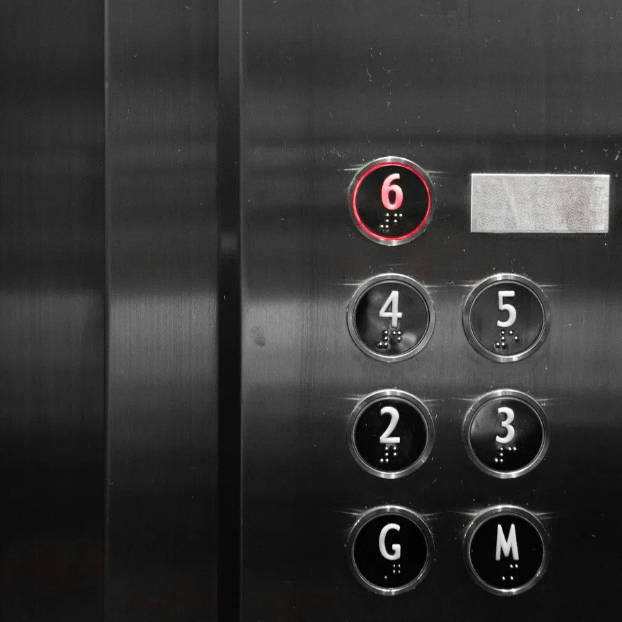 Elevator control panel with circular buttons numbered 2-6, G, M; button 6 is lit with a red ring.