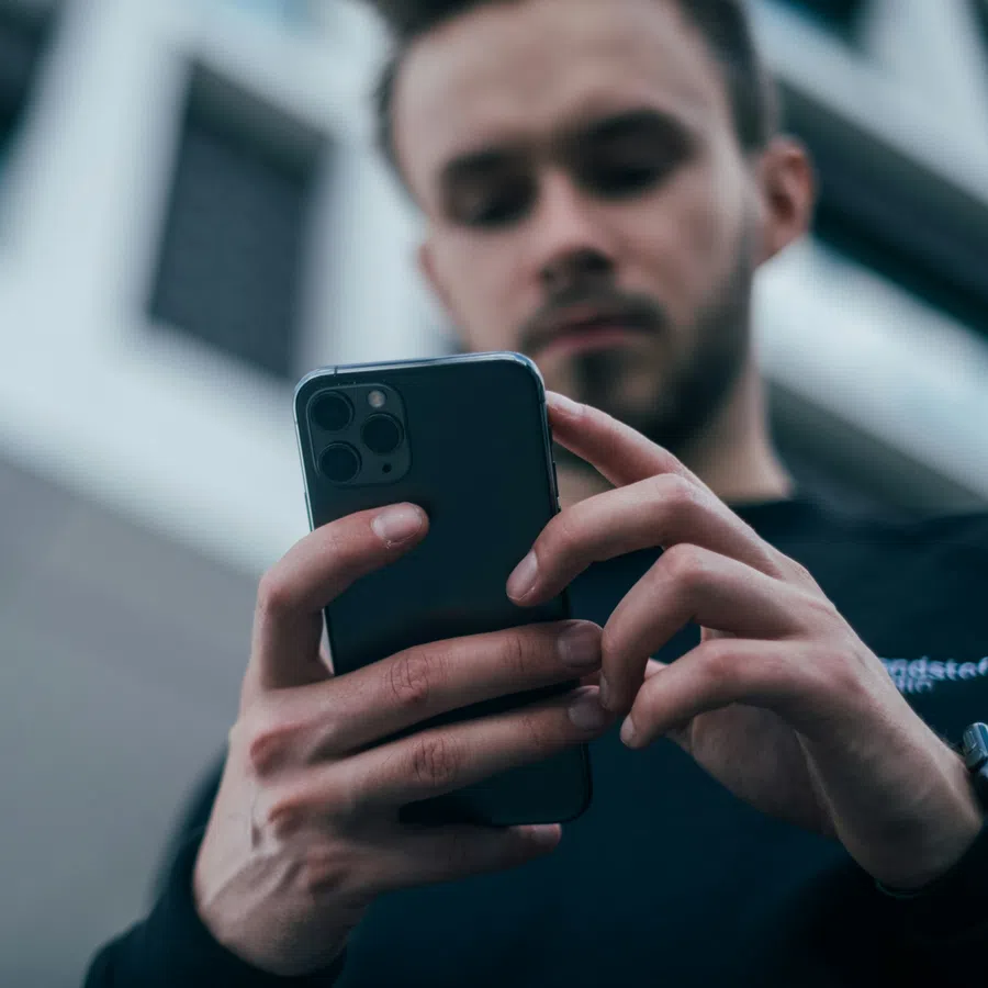 Man using a smartphone outdoors with blurred city buildings in the background.