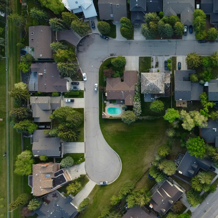Aerial view of a suburban neighborhood with houses, trees, roads, and a backyard swimming pool.