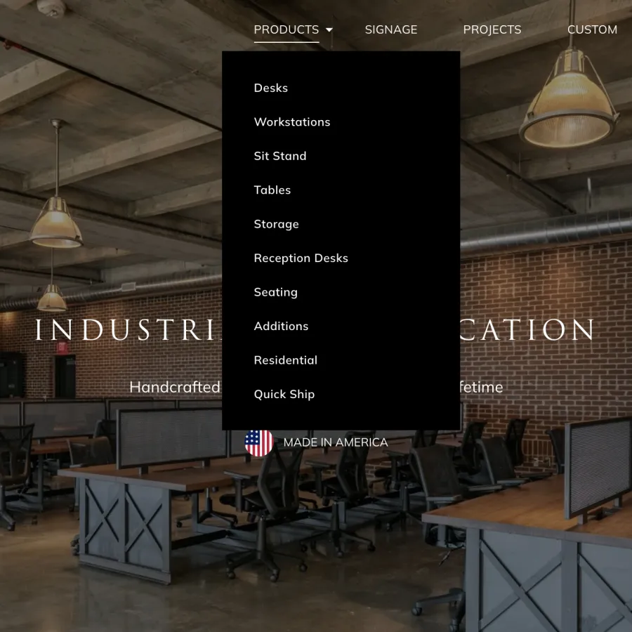 Industrial-style office workspace with wooden desks, black chairs, exposed ceilings, and brick walls under pendant lights