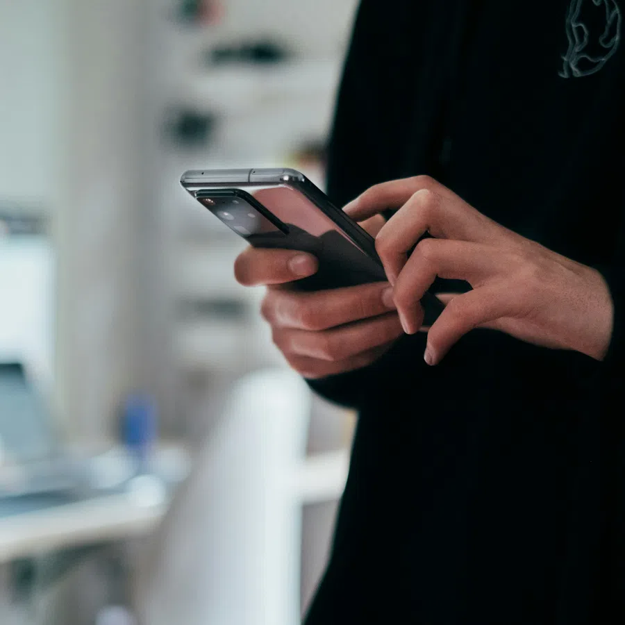 Close-up of person using smartphone indoors with blurred office background, focusing on hands and device interaction.