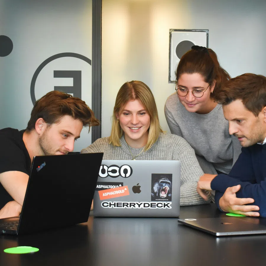 Four young professionals gathered around laptops collaborating in a modern office setting.