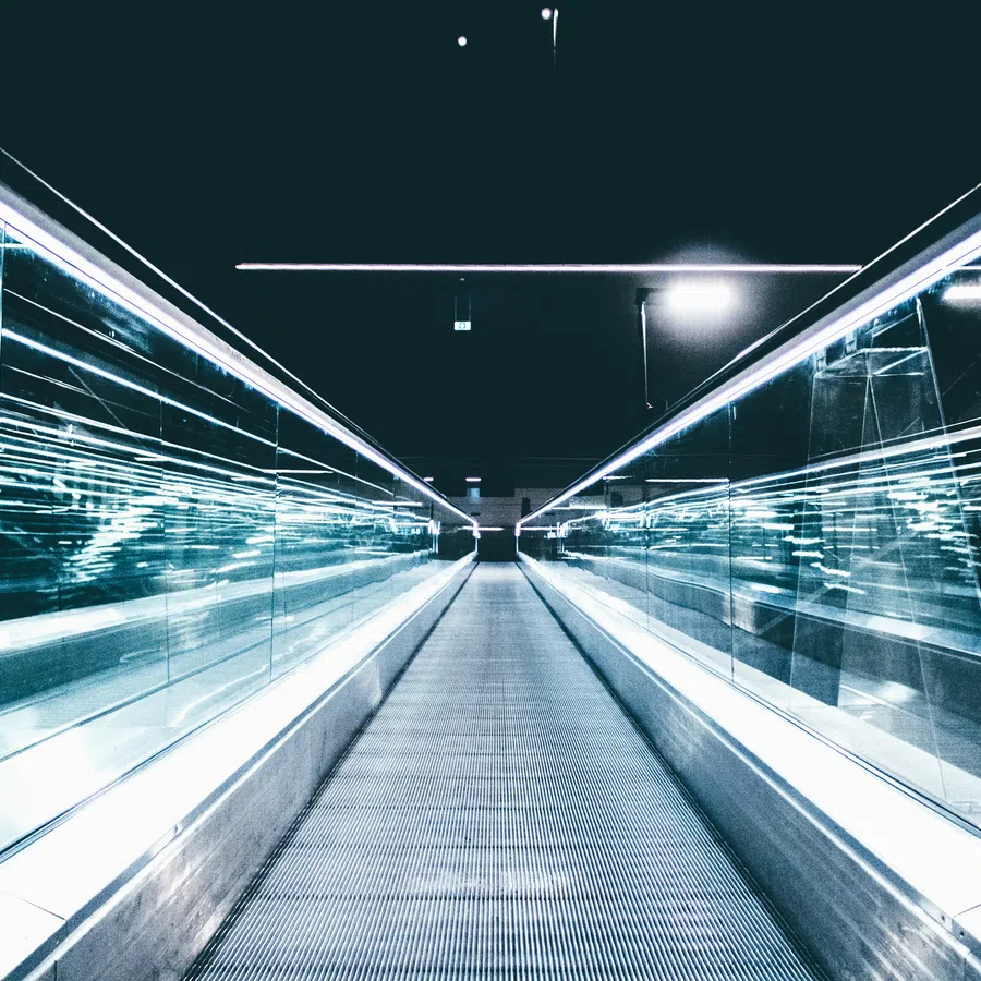 Futuristic illuminated walkway with glass sides and metallic floor in a dark modern setting.