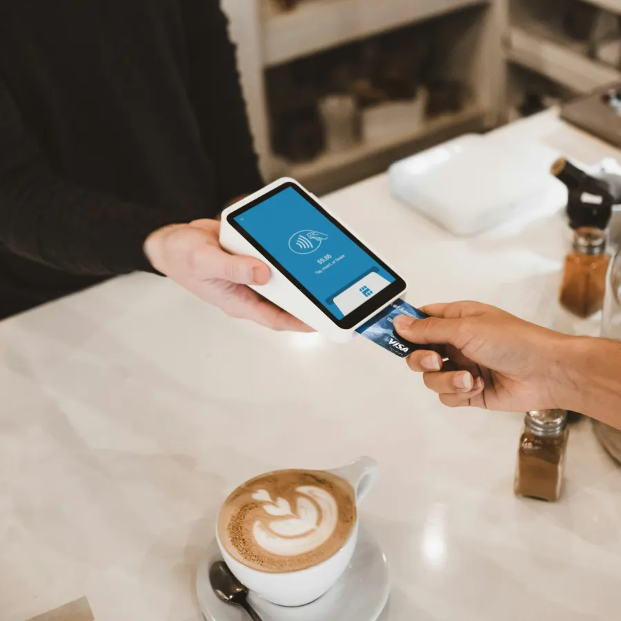 Customer making contactless payment with card at coffee shop counter beside a latte with latte art.