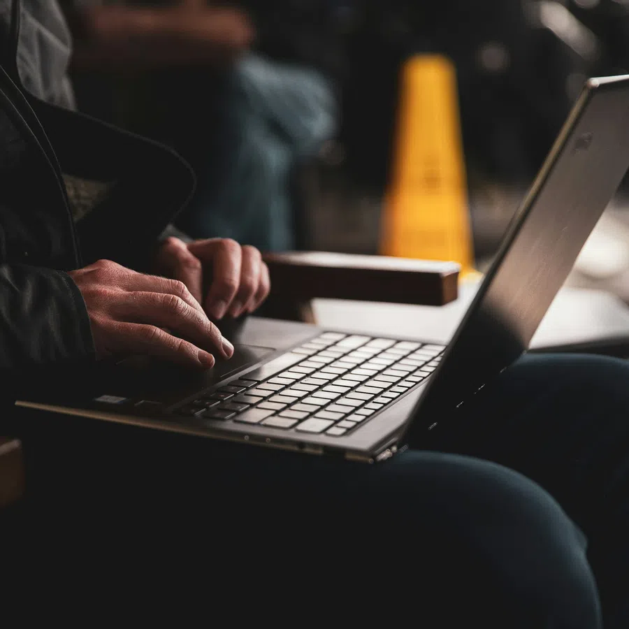 Person typing on a laptop keyboard while sitting in a dimly lit area with a blurred background.