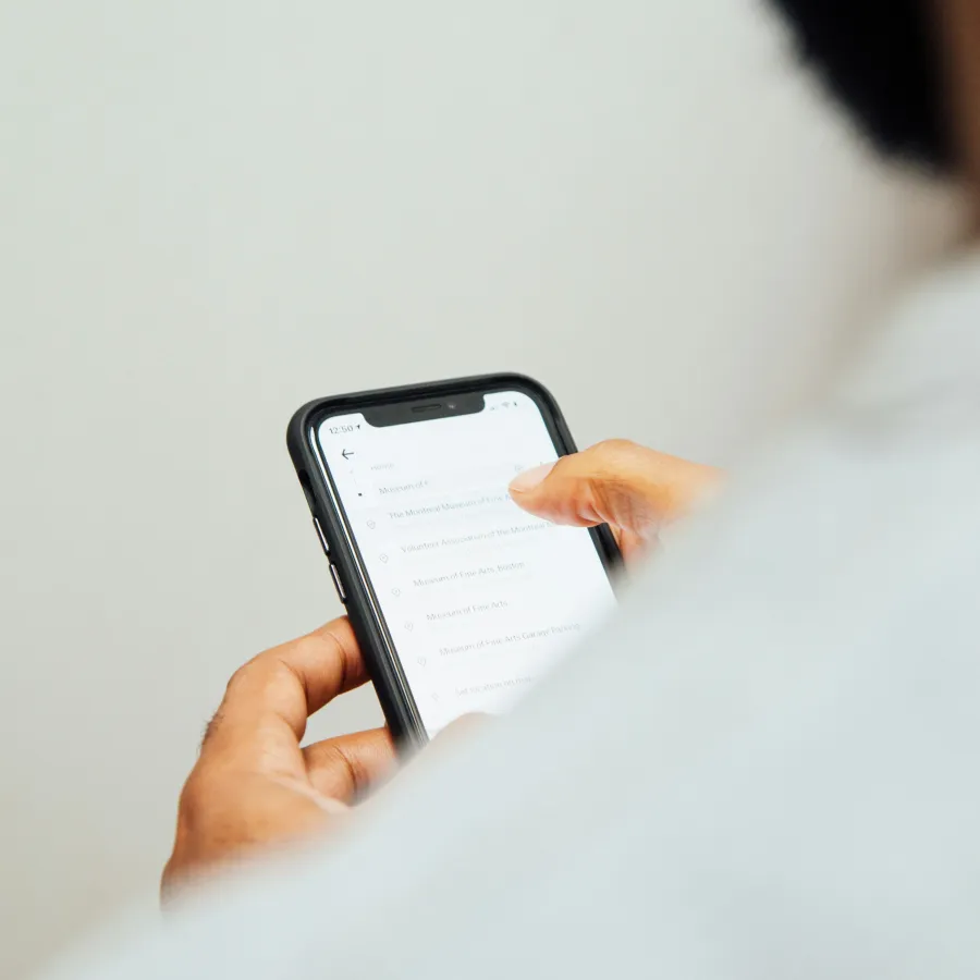 Person holding smartphone with location search results visible on screen in a minimalistic setting.