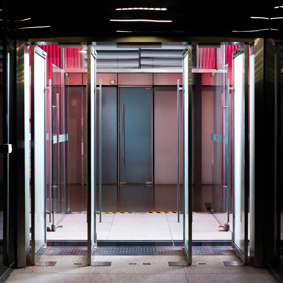 Modern glass revolving door entrance with metal frames and reflections in a dimly lit setting.