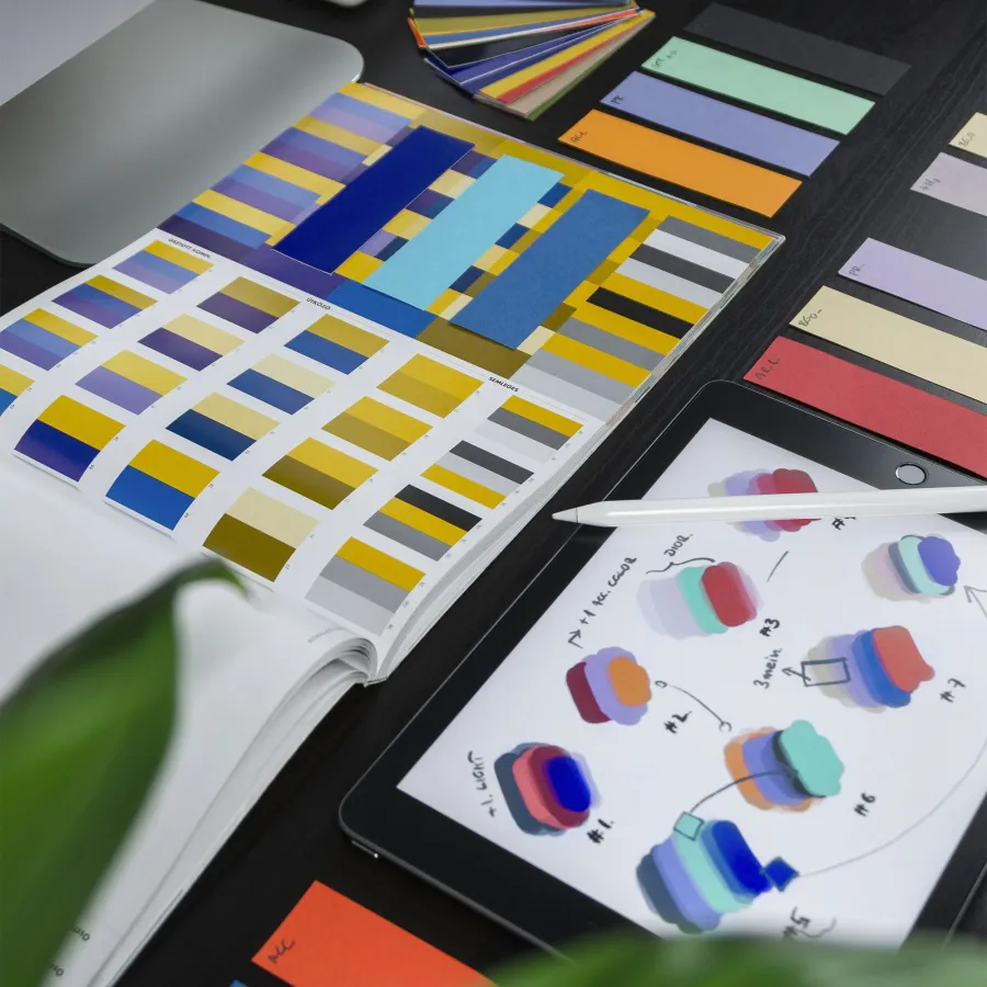 Workspace with color swatches, a tablet showing color concepts, and a silver iMac on a black desk.